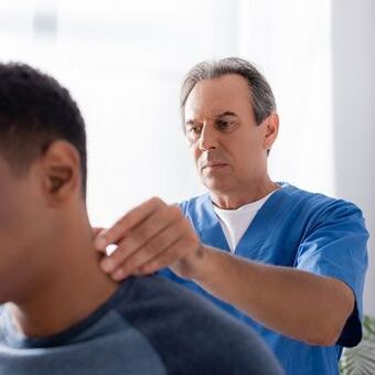 Gydytojas atlieka diagnostinį tyrimą pacientui, kuriam skauda kaklą.